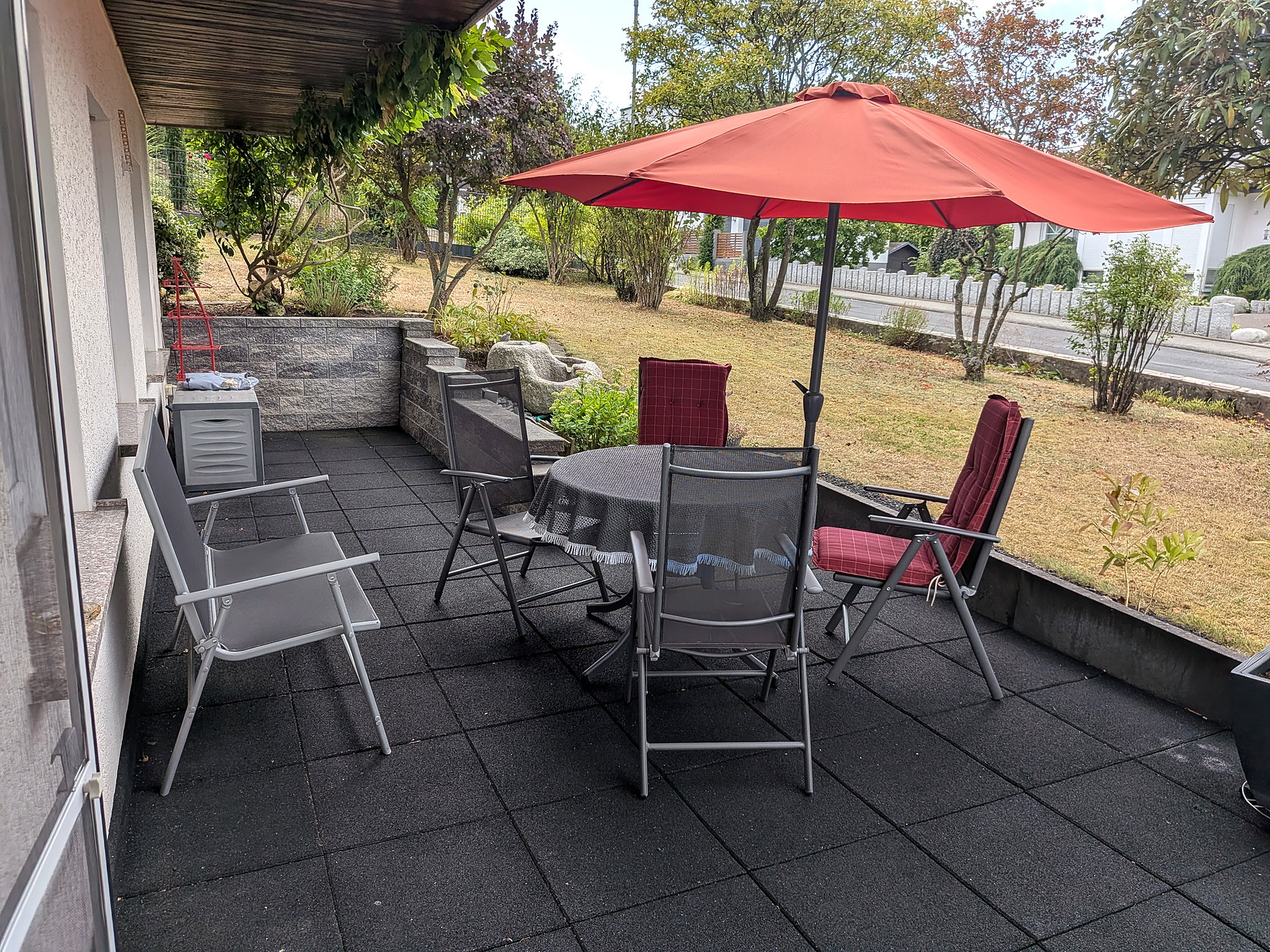Geschützte Terrasse mit Sitzgruppe und rotem Sonnenschirm